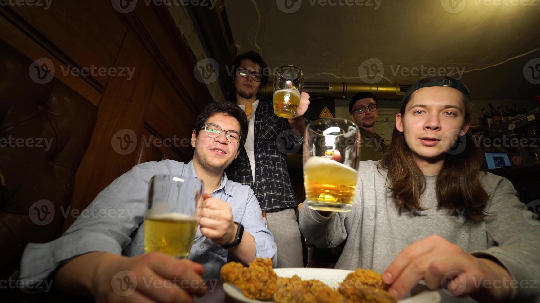 Young friends having fun together drinking beer and clinking glasses in a pub. photo