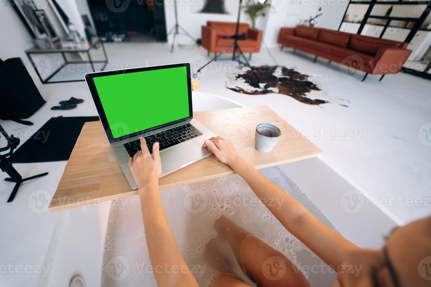 Young woman working on laptop while taking a bathtub photo