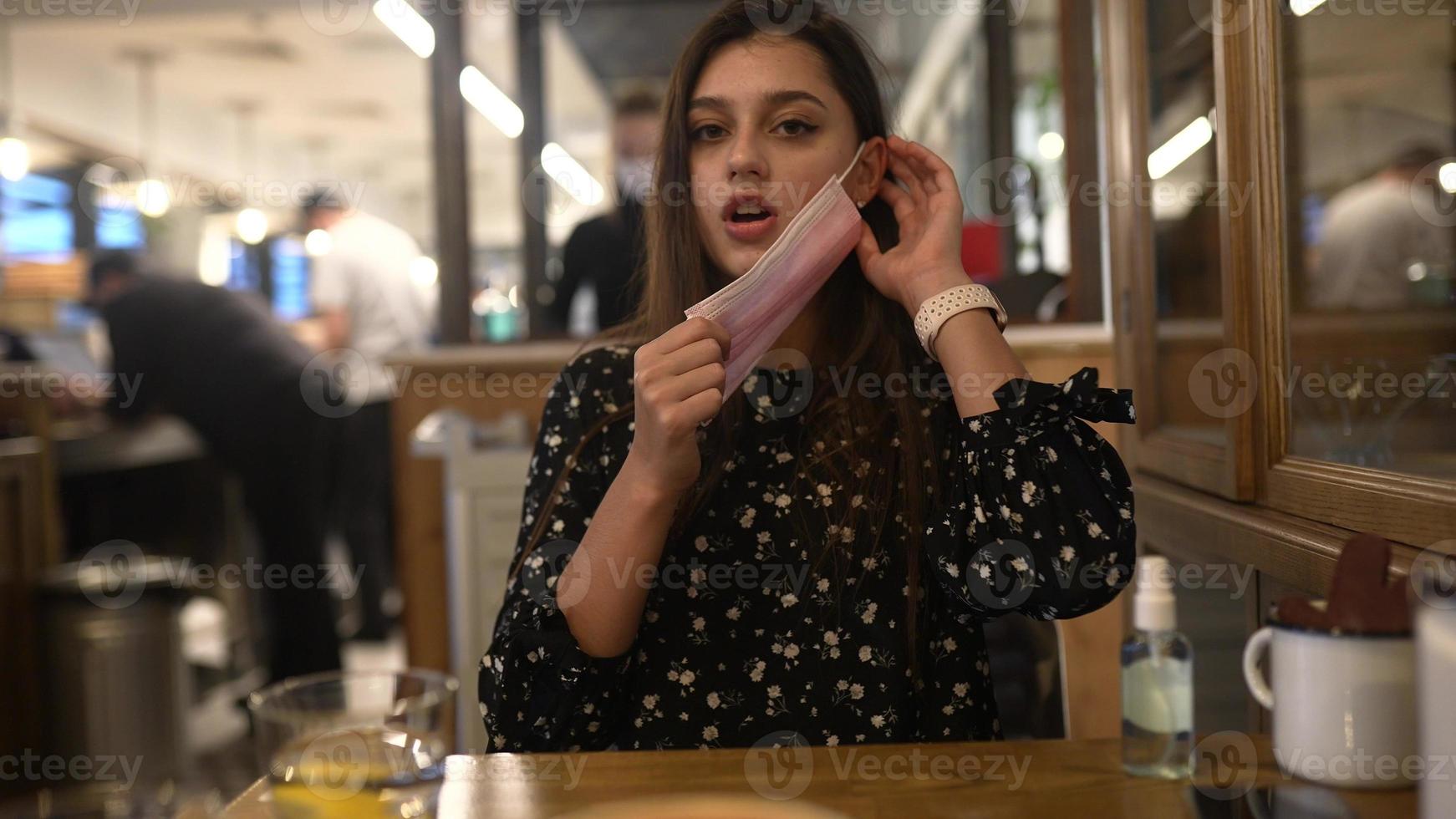 Attractive young woman putting on protective mask in the cafe. photo