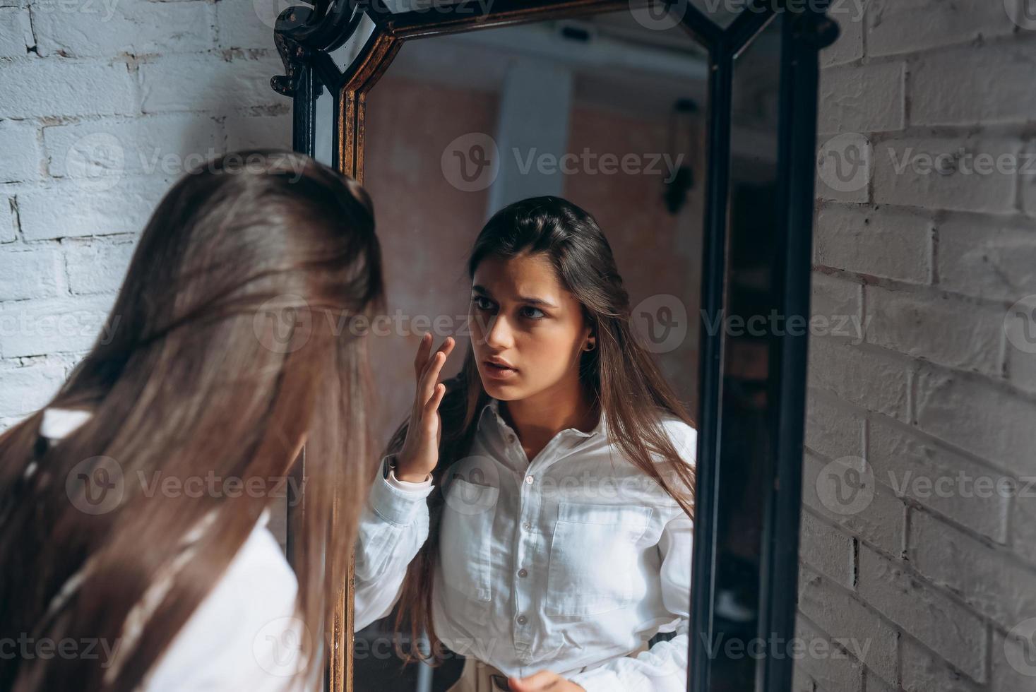 Young woman carefully looks in the mirror. photo