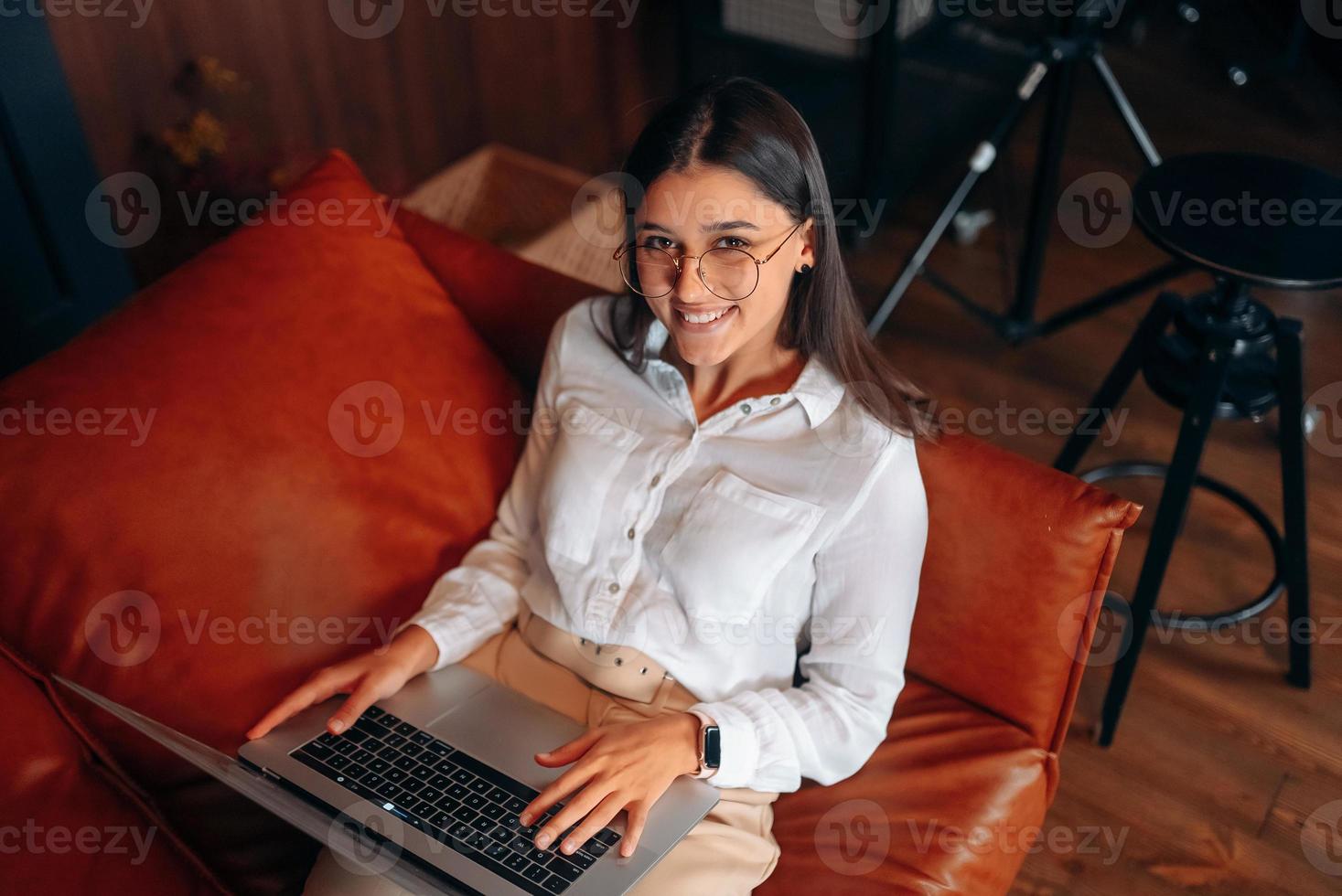 Young woman sits on a red sofa while working at a laptop. photo