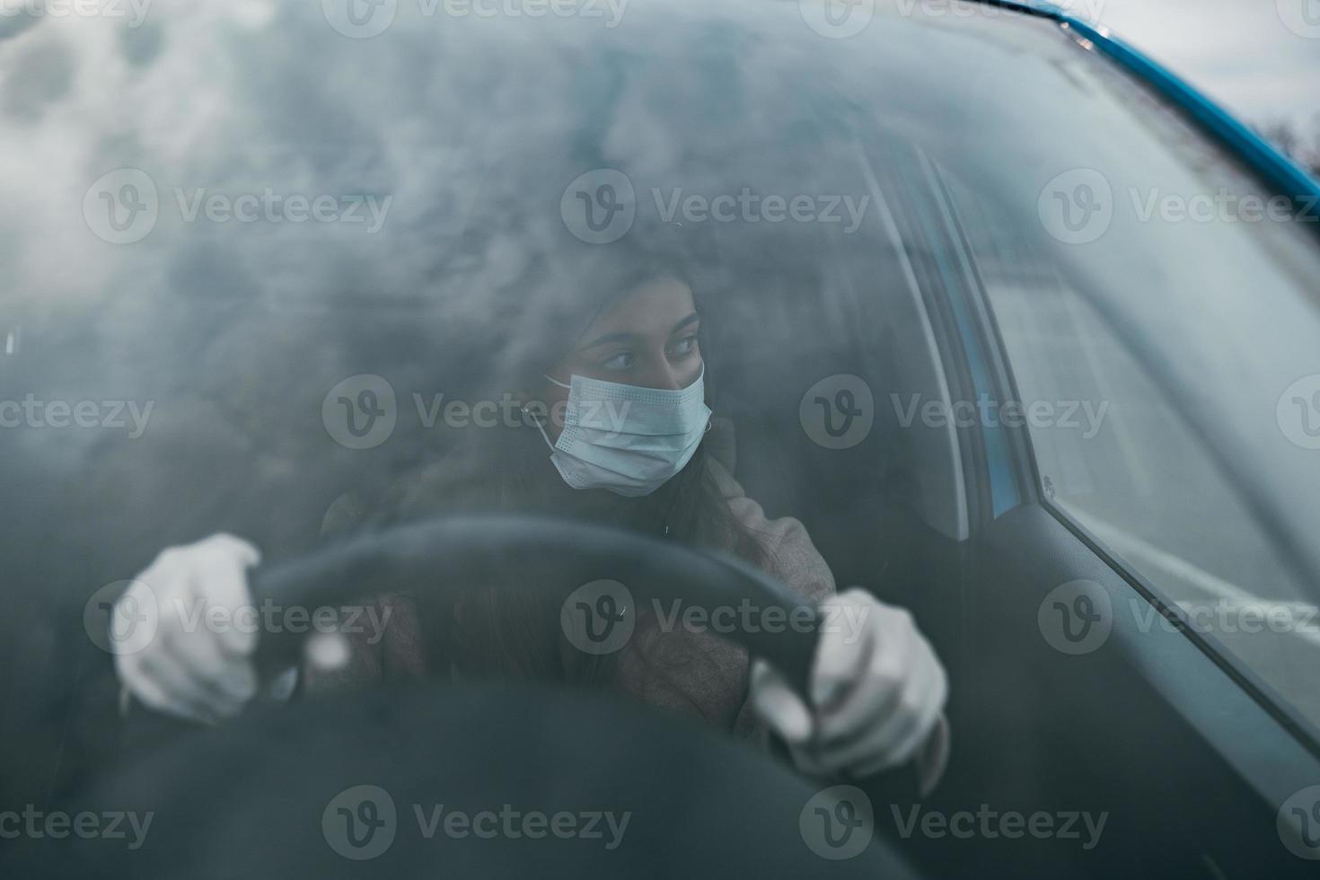 mujer joven con una máscara y guantes conduciendo un automóvil. foto