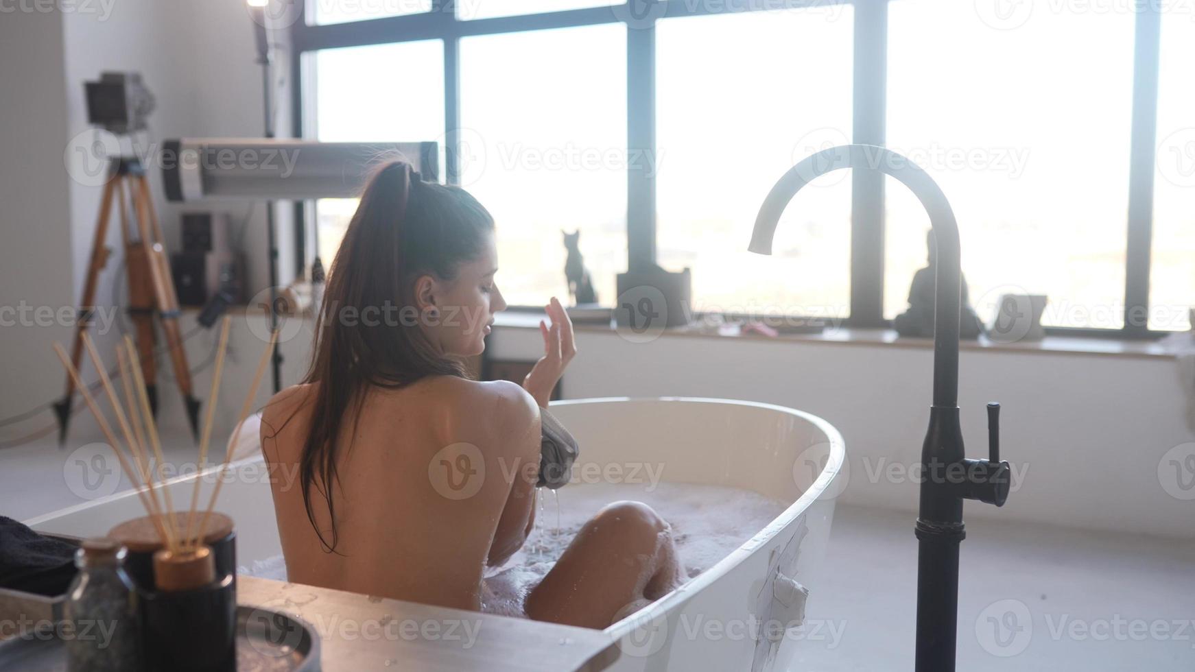 Beautiful woman washes her arm with a sponge while taking a bath photo