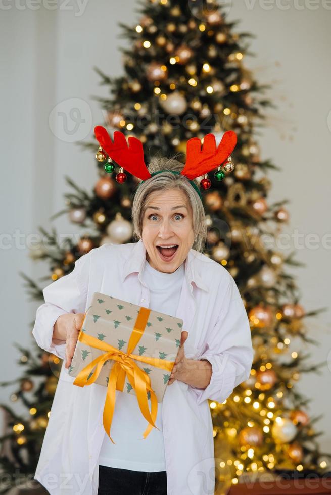 Grandma wearing deer christmas hat. Christmas present in hand . photo