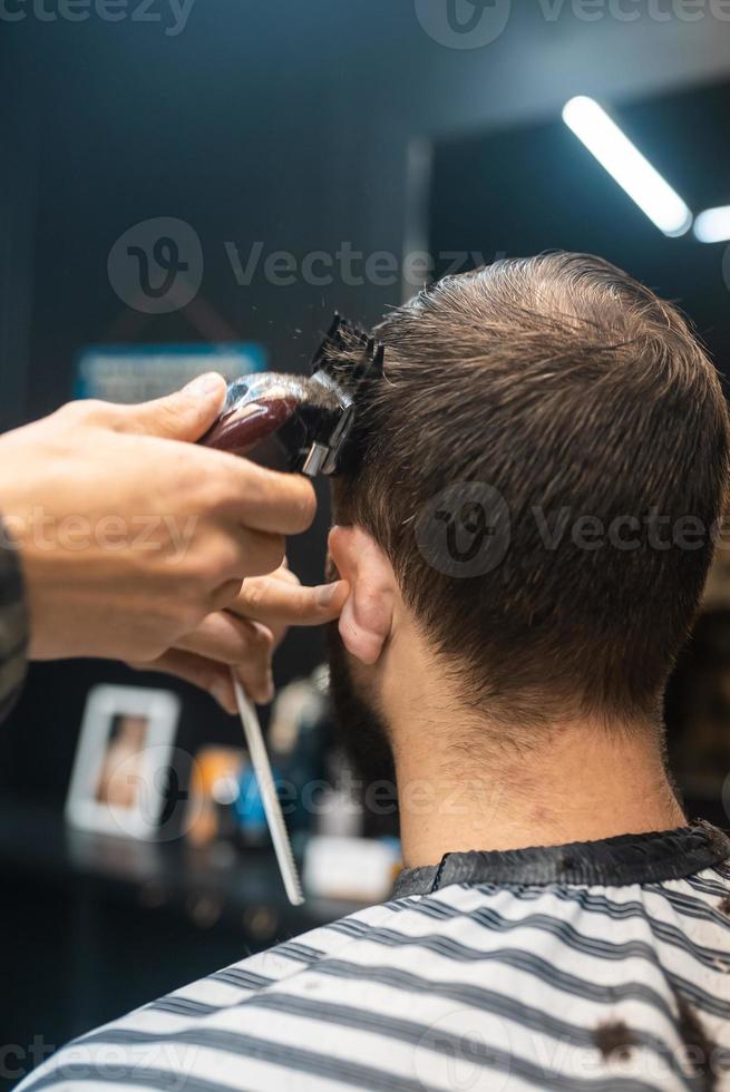 Master in barbershop makes men's haircutting with hair clipper photo