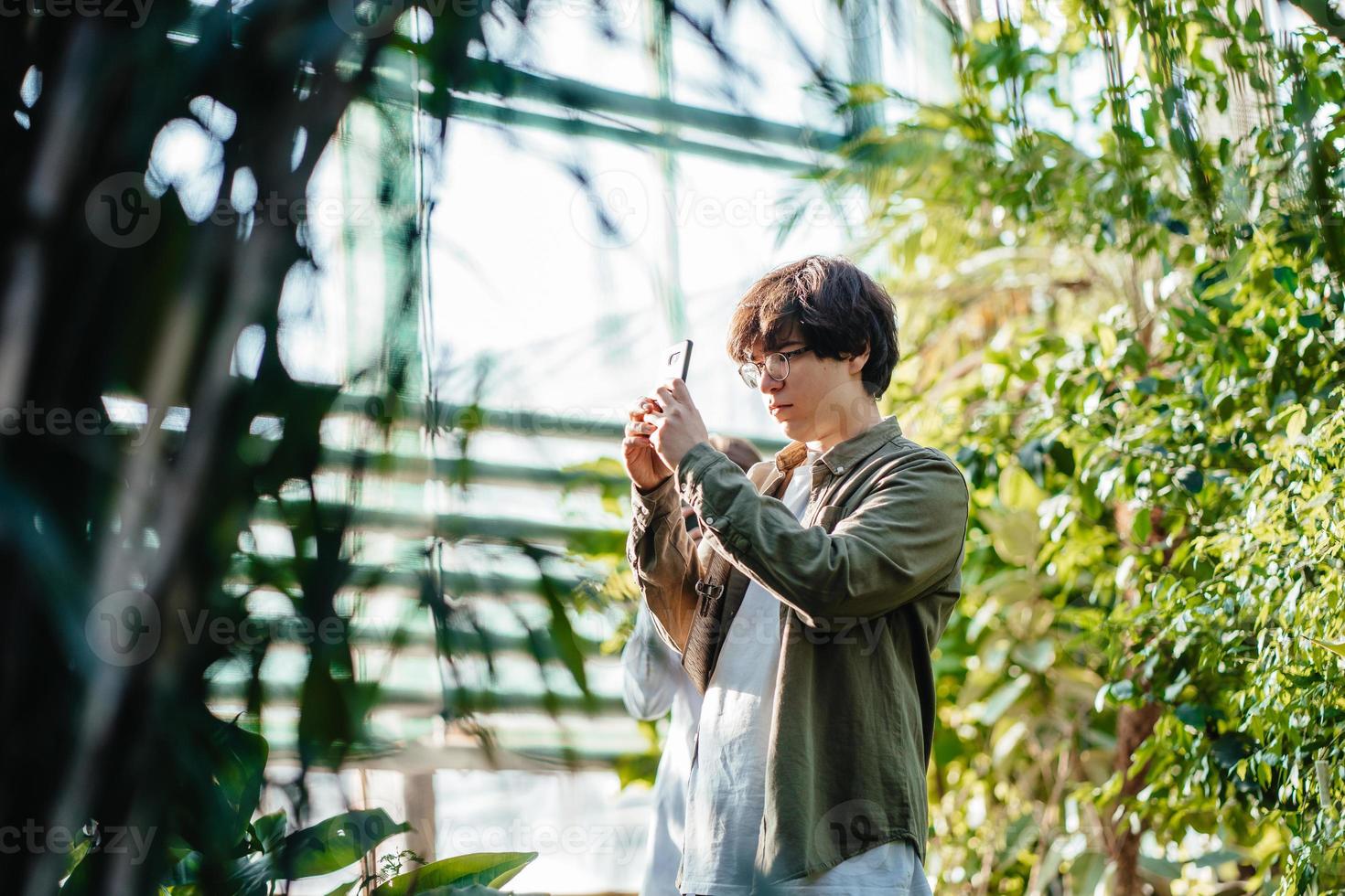 Young agricultural engineer working in greenhouse. Male scientist take a foto photo