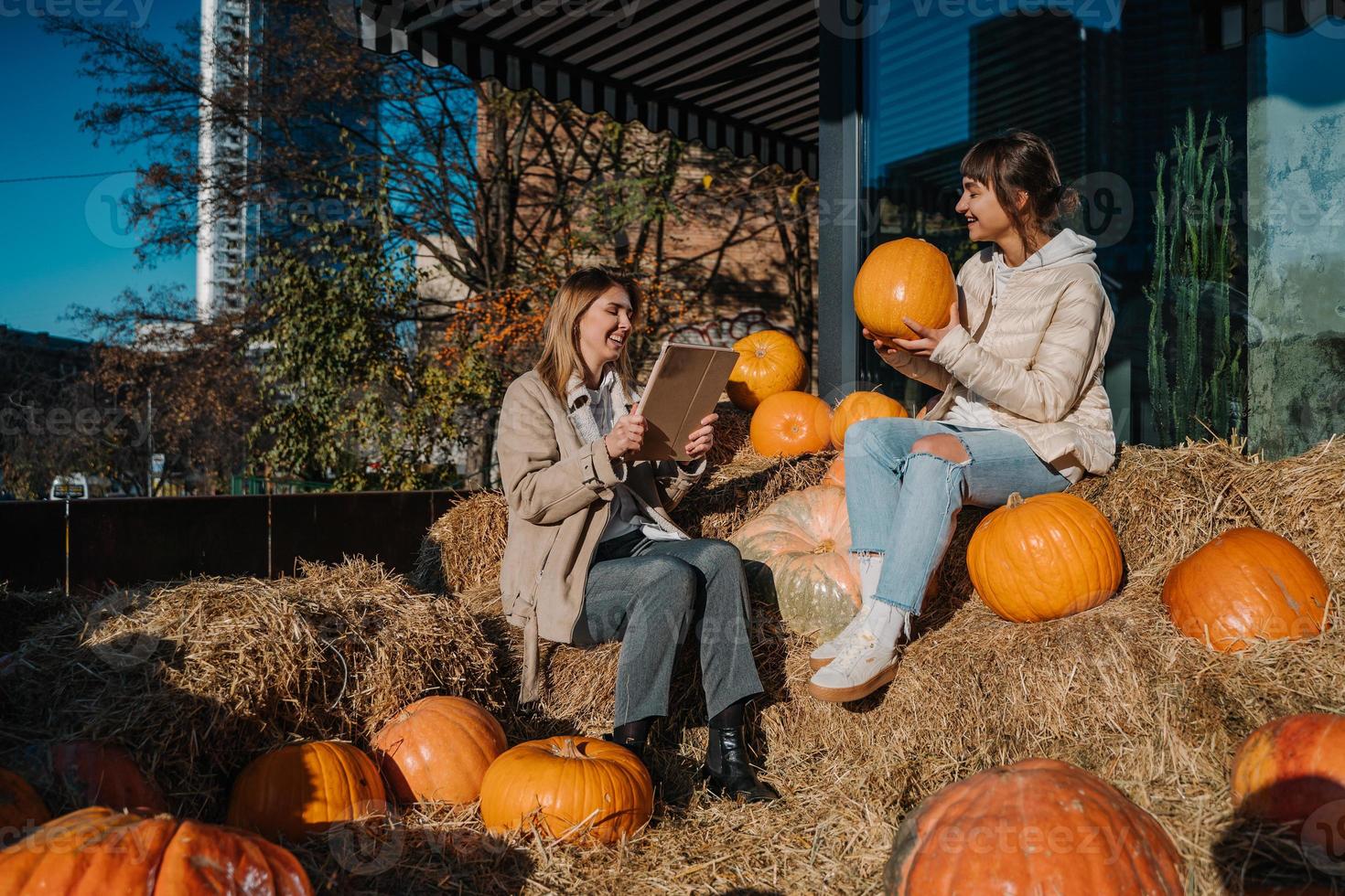 Girls have fun among pumpkins and haystacks on a city street photo