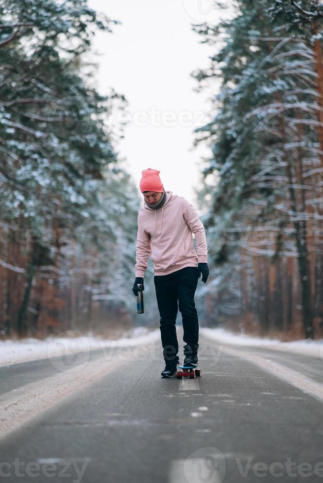 Skateboarder standing on the road in the middle of the forest, surrounded by snow photo