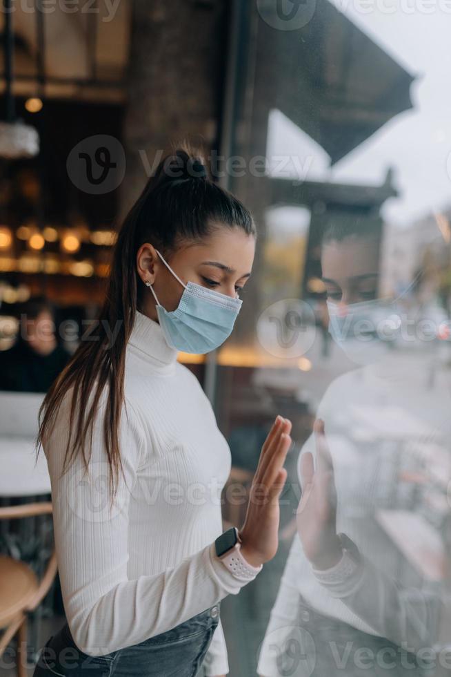 Young woman in face mask standing in front of windows in cafe. photo