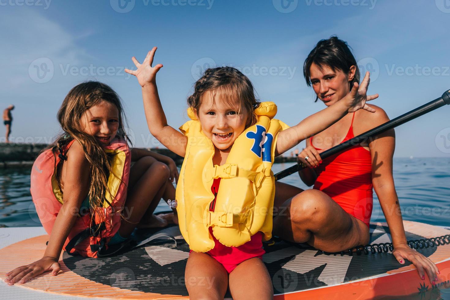 Mother with two daughters stand up on a paddle board photo