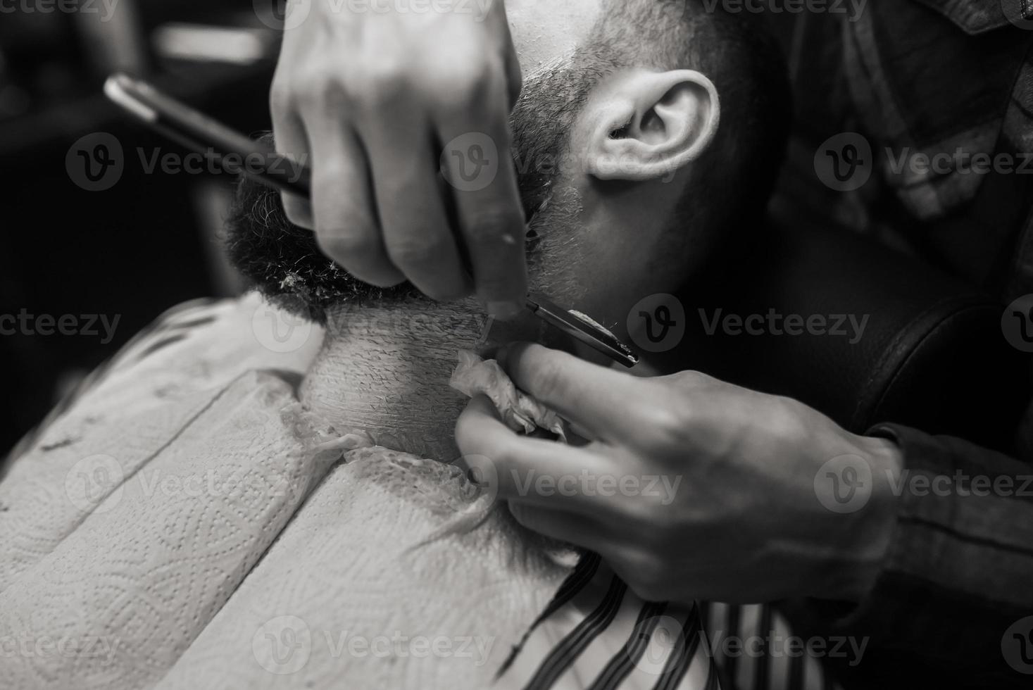 joven barbudo siendo afeitado por el peluquero en la barbería foto