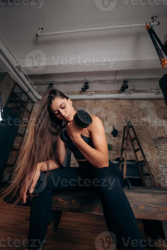 mujer joven bombea los músculos con un brazo levantando pesas. foto