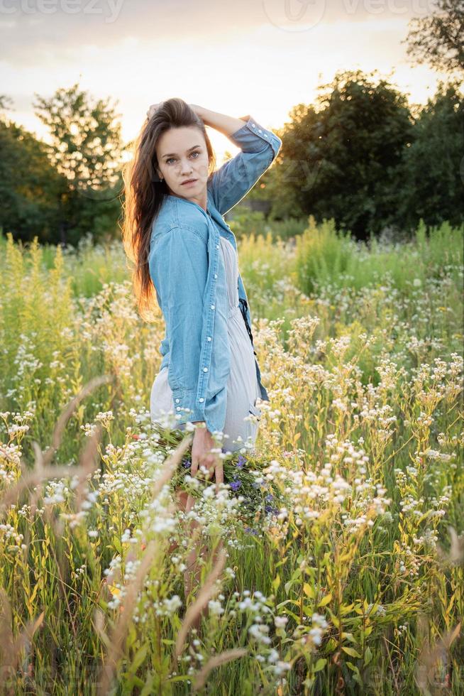 hermosa chica caminando en el campo en verano con flores silvestres. foto