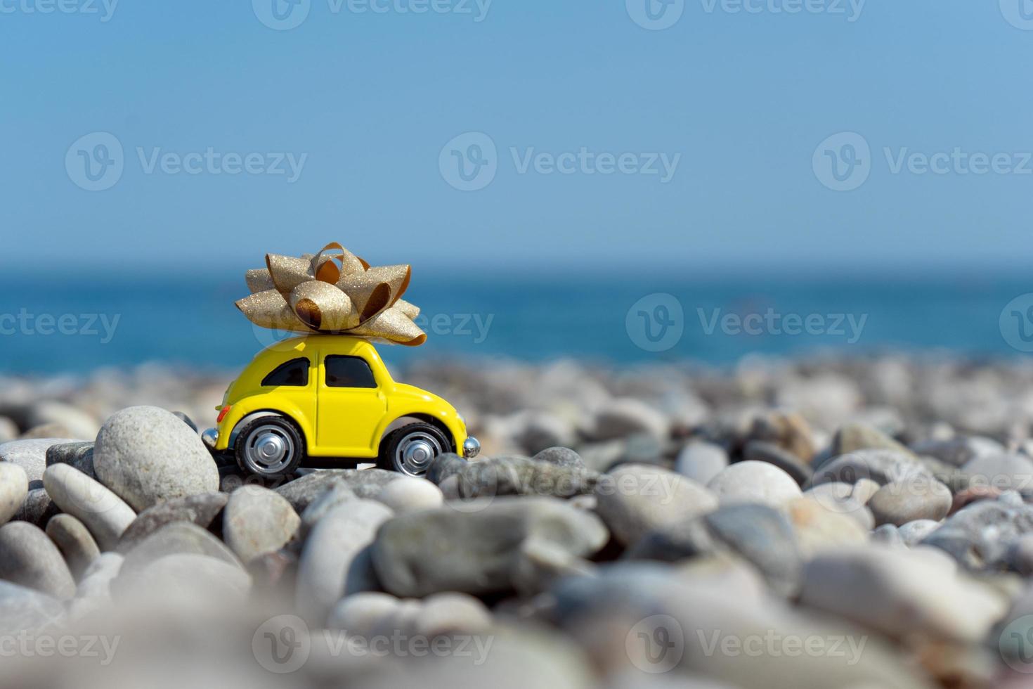 A yellow car with a bow on its top standing on the seaside photo