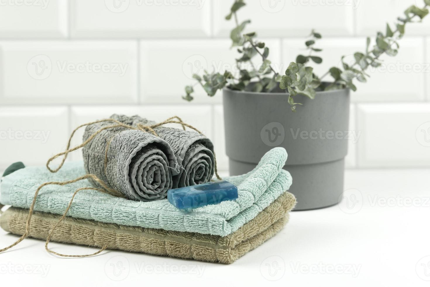 Cotton towels of neutral colour with a branch of eucalyptus on them lie on a table in a modern bathroom photo