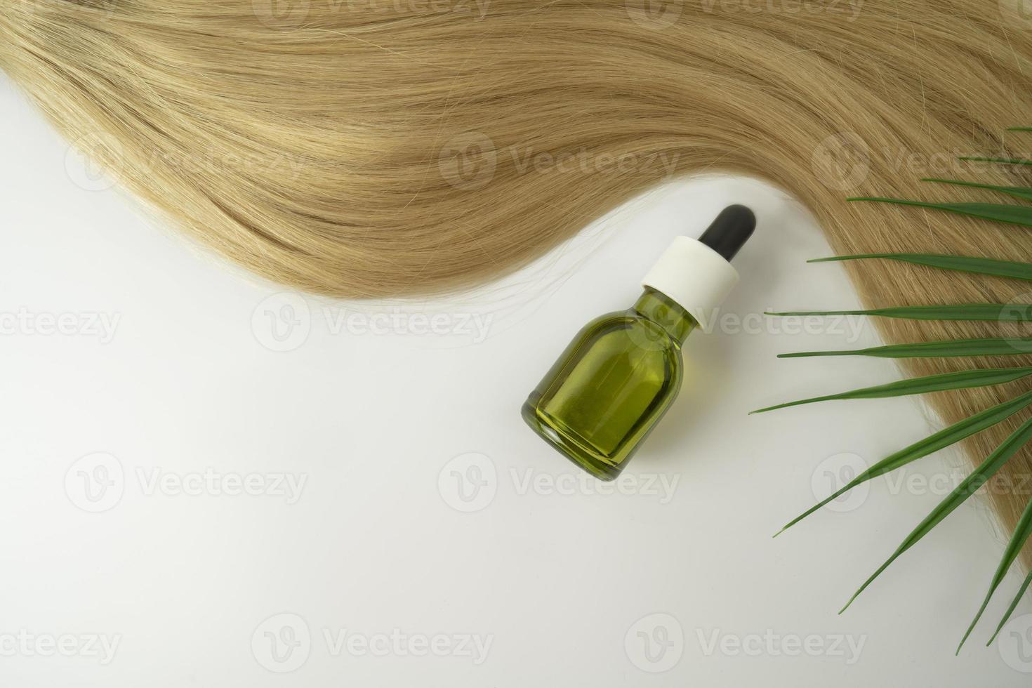 A natural oil or serum for hair care and a ply of blonde hair lying on a white background photo