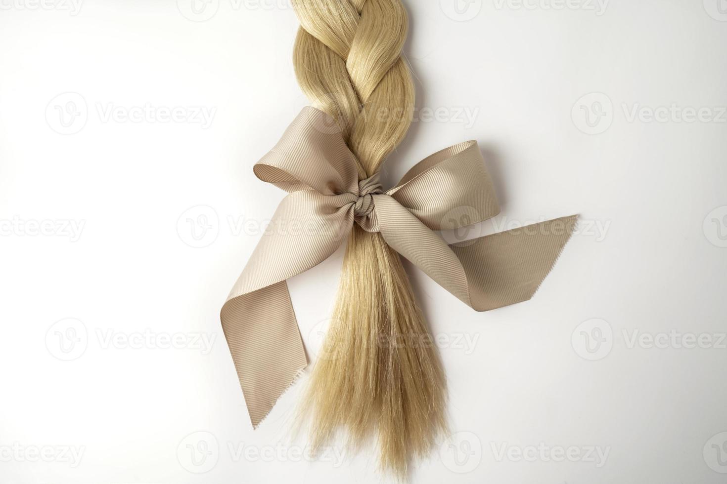 A blonde tress with a beige bow on a white background photo