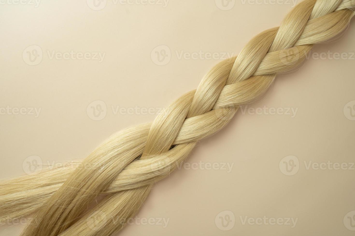 Woman's long blonde hair in the form of the tress lying on a beige background photo