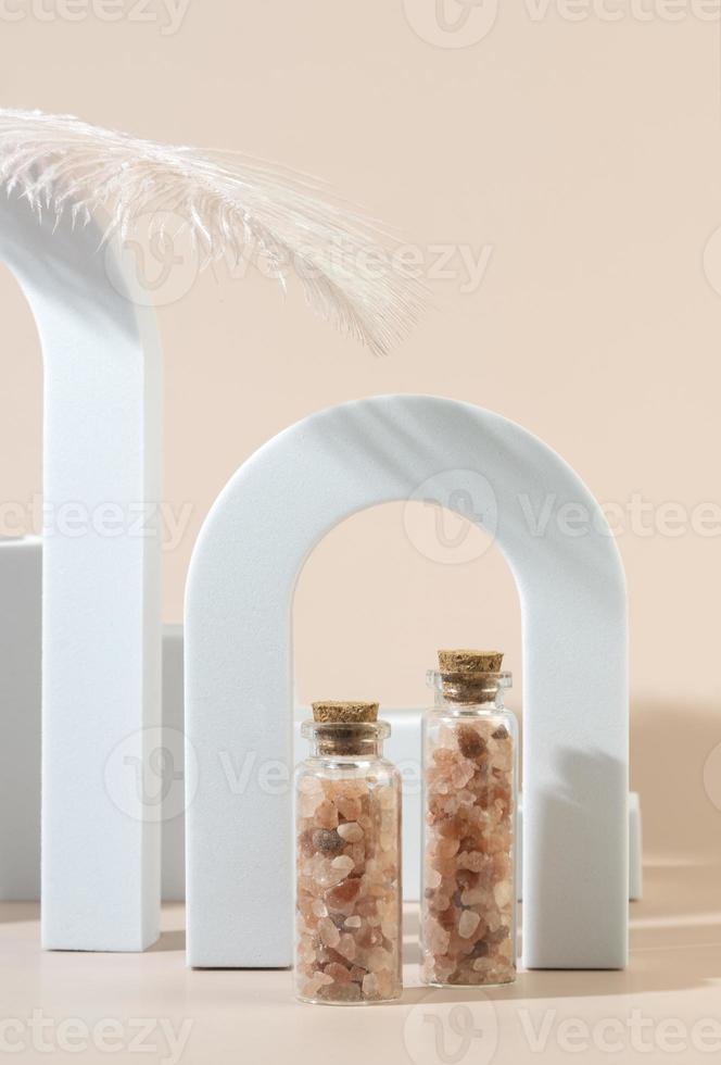 Two glass bottles with pink sea salt for spa procedures for face or body standing between geometric forms photo