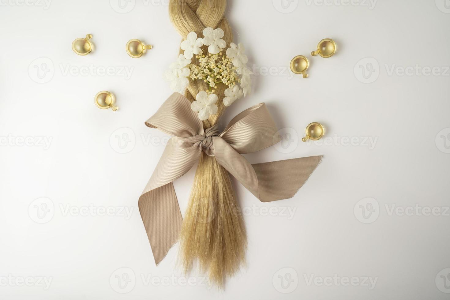 una trenza rubia con un lazo beige y vitaminas de aceite para el cabello foto