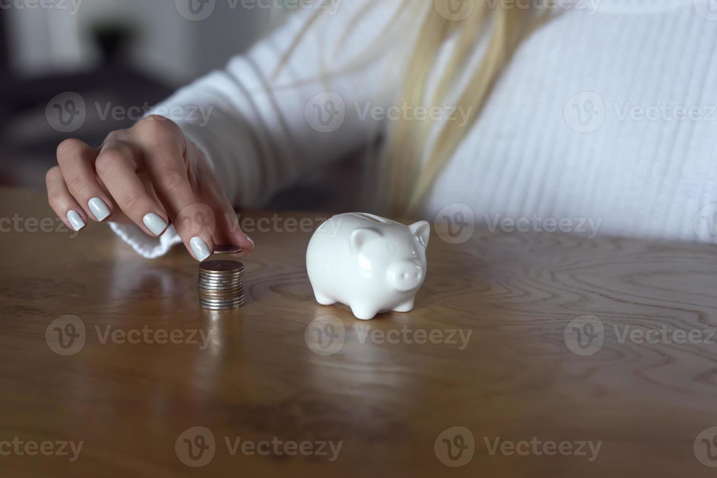 A woman puts a coin into a piggybank for saving purposes photo
