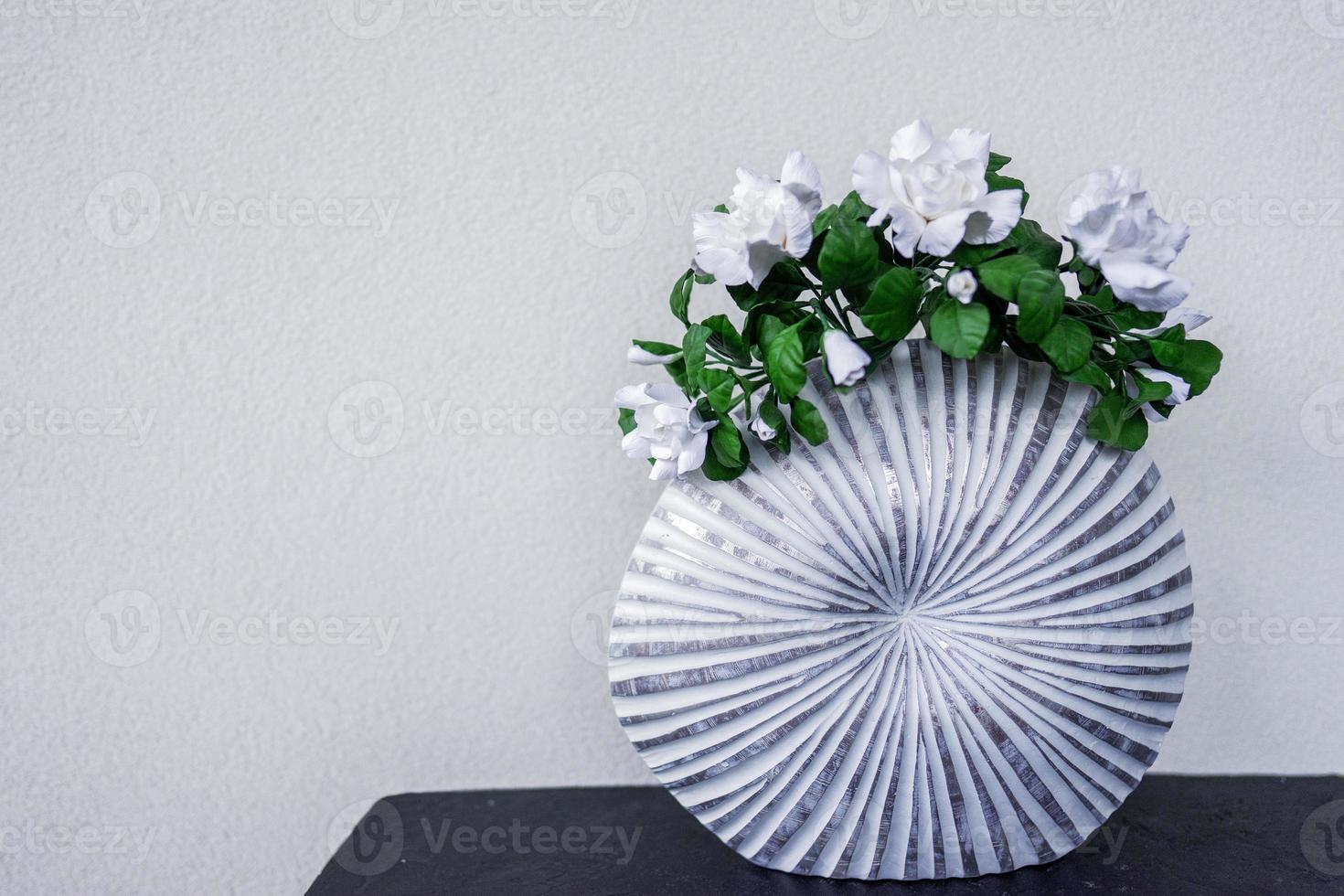 Flowers in a vase stands on the table as a part of the decor in the modern apartment. Textured white wall background photo