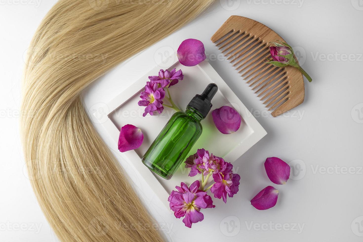 A hair care oil or serum in green dropper bottle lying on a white ceramic tray with rose petals around it, product marketing mockup. A concept of hair care in a salon or at home photo