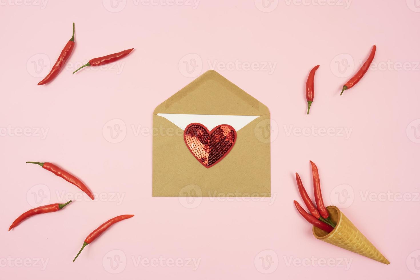 Red hot chilli peppers with a brown envelope with a red lie on a pink background table. Copy space. photo