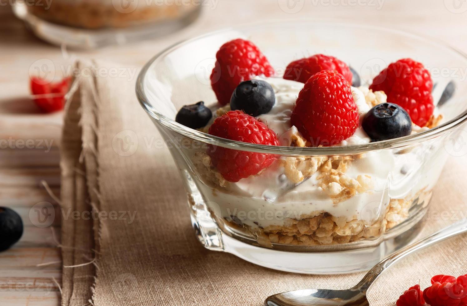 Raspberries, blueberries, cereals and yogurt in a glass bowl on sackcloth and wooden slats. Healthy breakfast for a healthy life. Horizontal image. photo