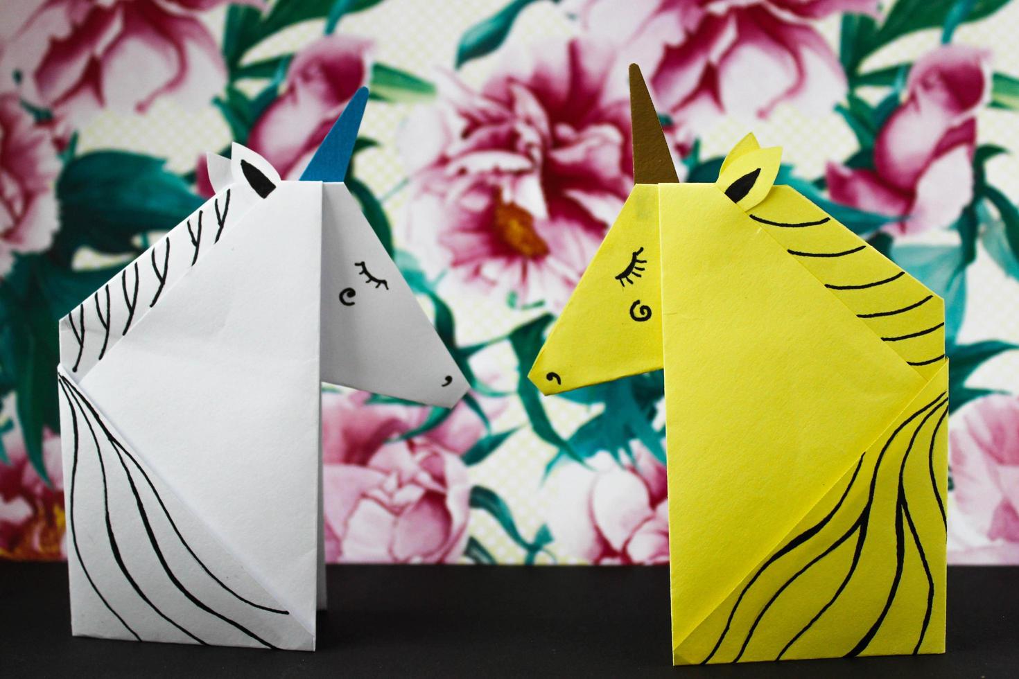 unicornios blancos y amarillos hechos en la técnica del origami sobre fondo de flores. foto