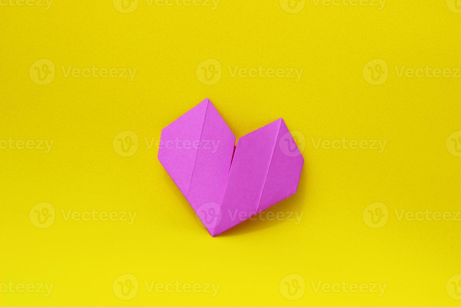 Purple paper origami heart on a yellow background in the center of the photo. Minimalistic background photo