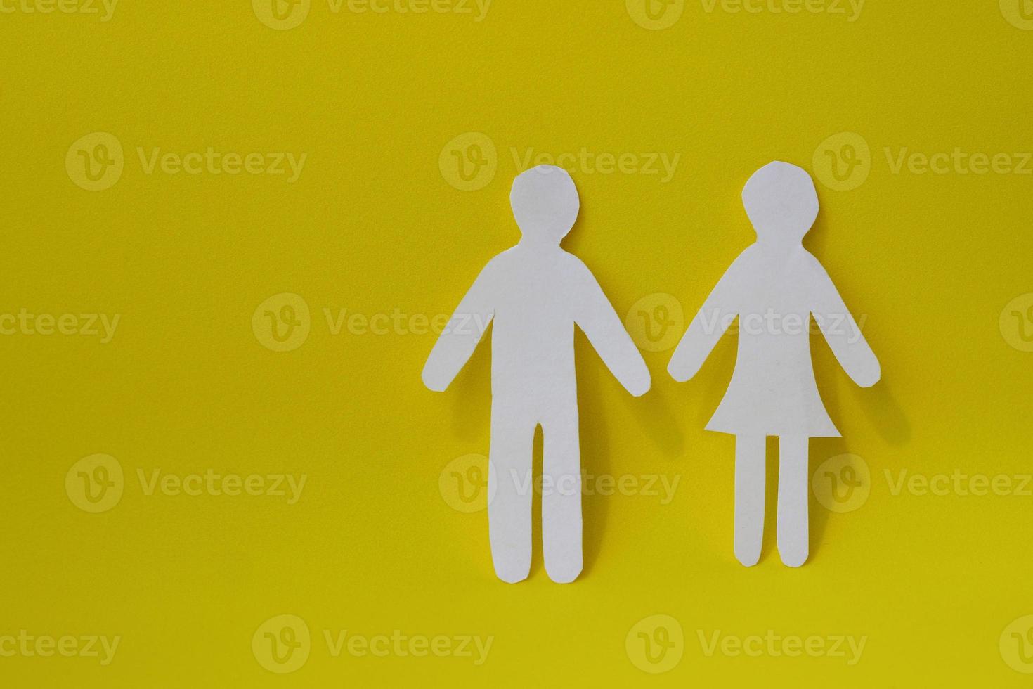 Silhouettes of a man and a woman are carved from white paper, standing side by side on a yellow background. With copy space. The concept of love, relationships, family photo