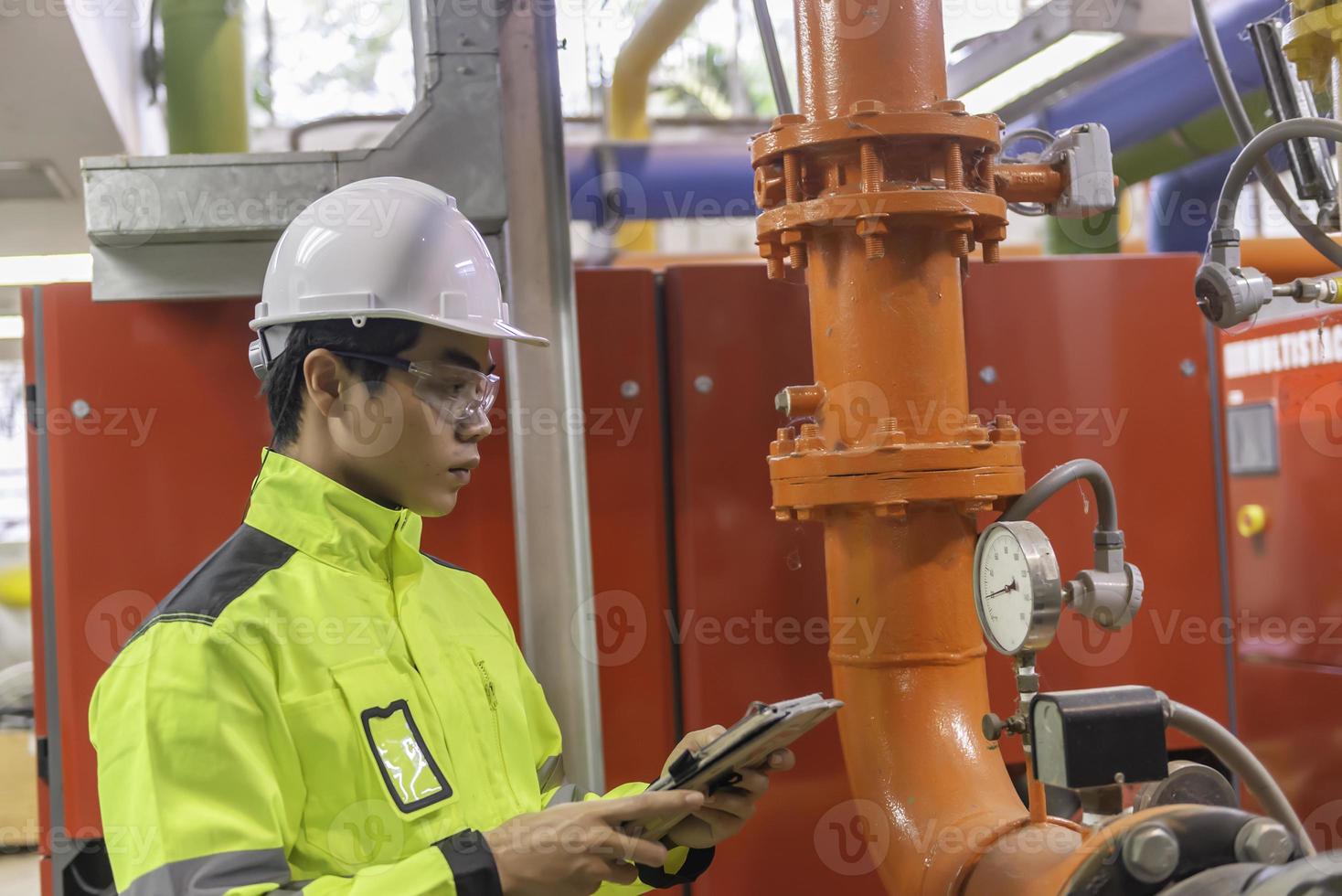 Asian engineer wearing glasses working in the boiler room,maintenance checking technical data of heating system equipment,Thailand people photo