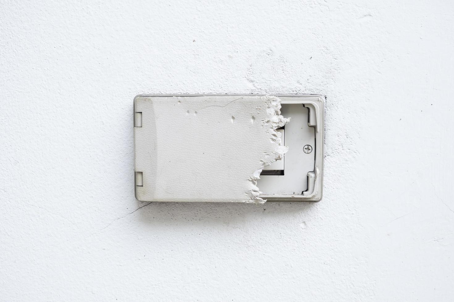 Electric plug cover was dog bite. Wall cover plug socket damage. Outdoor electric outlet on white wall. photo