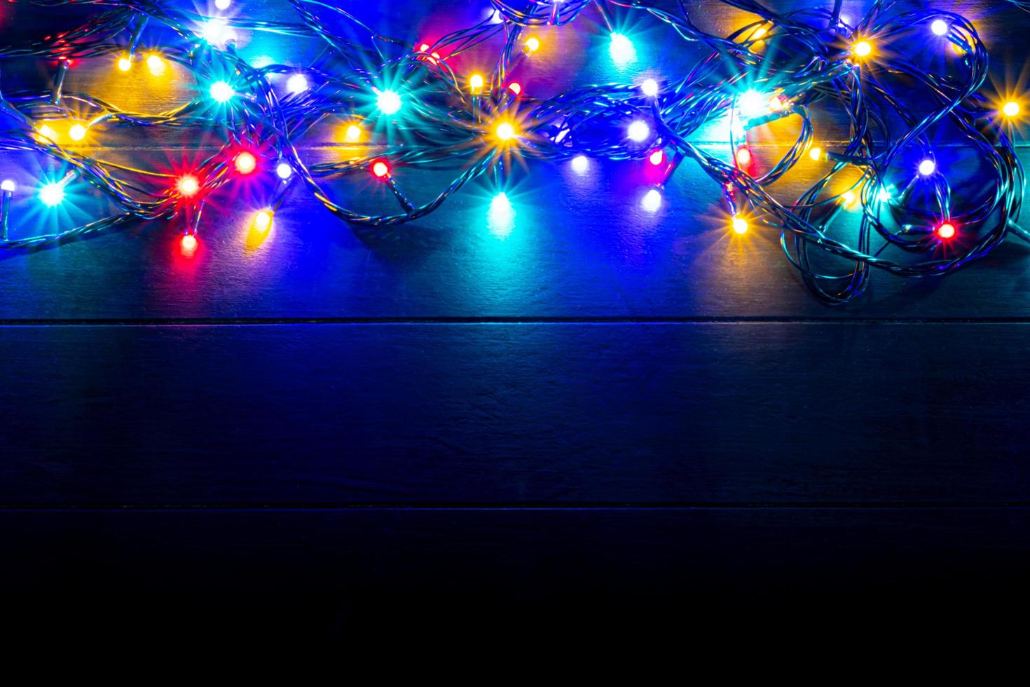 Christmas lights background with free text space. Glowing colorful Christmas lights on wooden background. New Year. Multi color lights for decorate event. photo