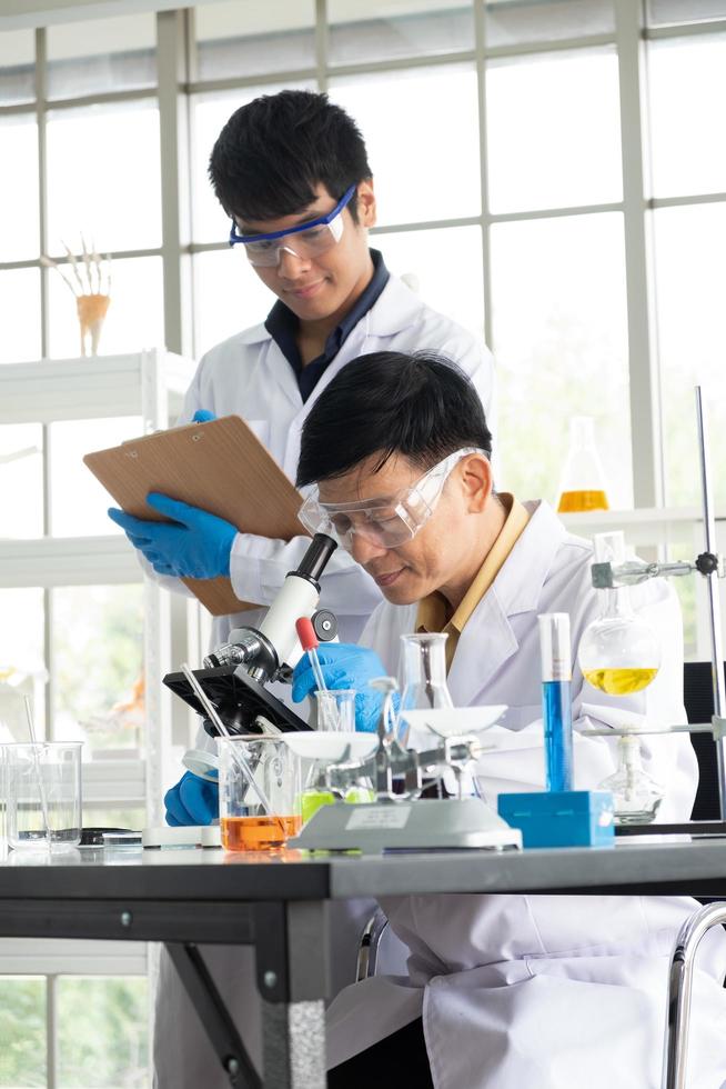 Science, Chemistry, Technology, Biology and Laboratory concept - Asian Senior scientist looks into something on a petri dish while Asian junior scientist taking notes. photo