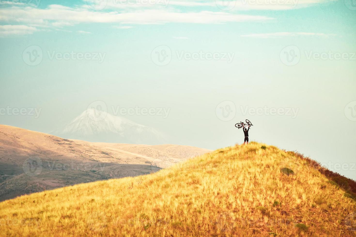 Caucasian cyclist lift bicycle up on top viewpoint inspired in mountains after reaching top. Achievement , inspiration, challenge and determination concept photo