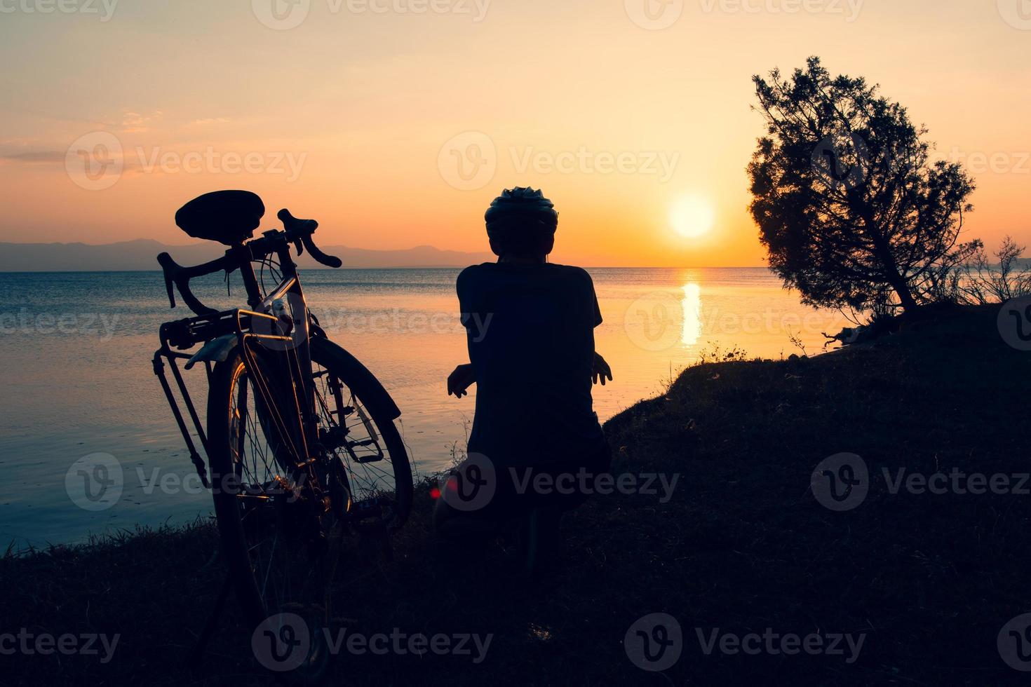 Inspirational view caucasian male cyclist sit by touring bicycle looking to scenic relaxing golden sunset background by sevan lake in Armenia. Bicycle touring lifestyle concept photo