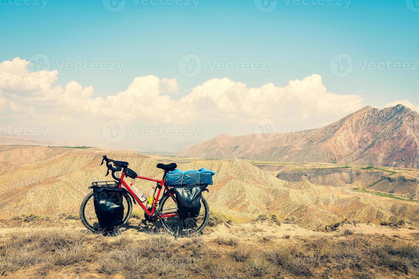 Loaded touring bicycle stands with moody dramatic panoramic mountains view and no cyclist photo