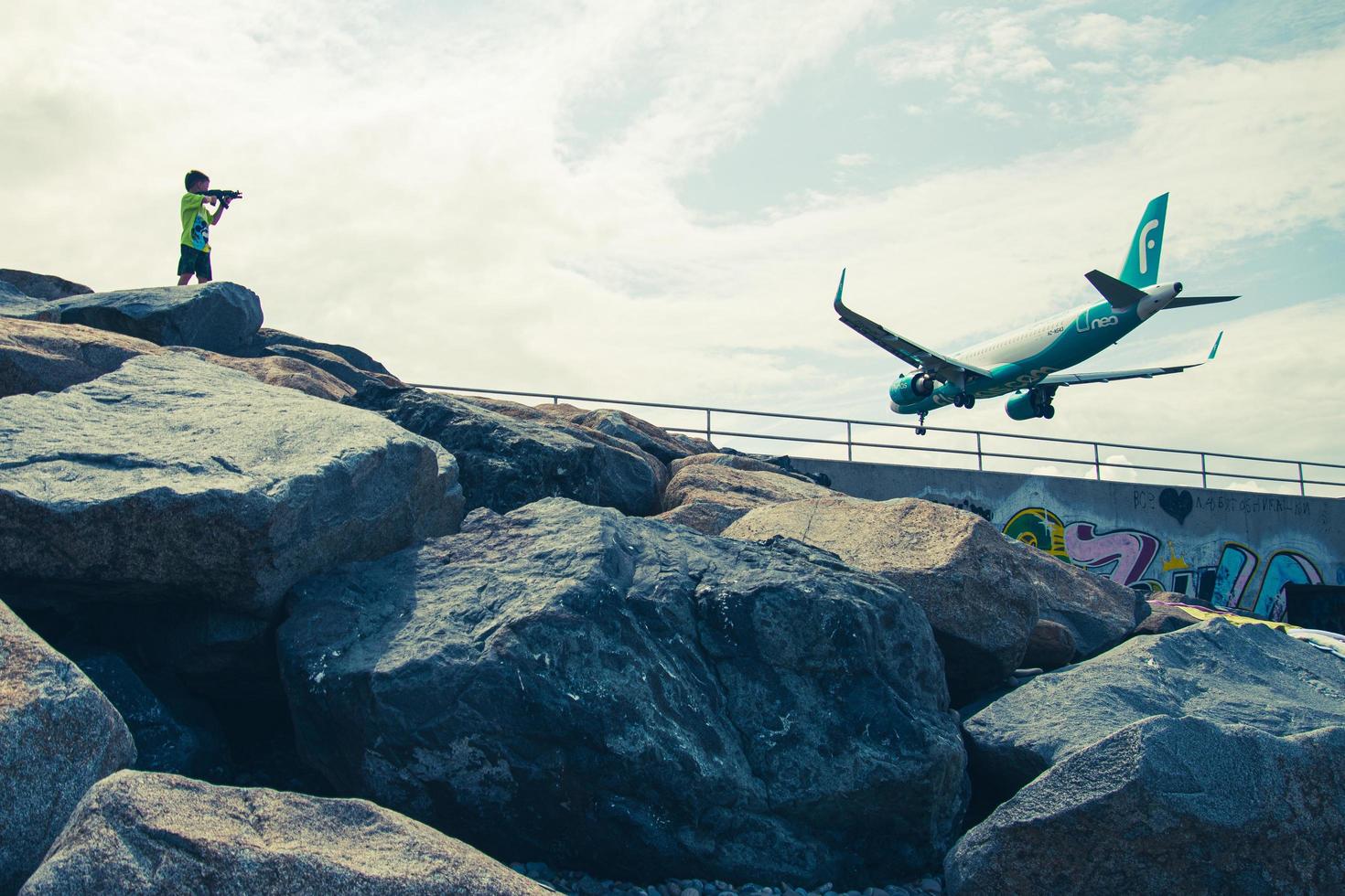 batumi, georgia, 2022 - turista de vista trasera en un niño de la playa con un disparo de pistola de juguete a un avión comercial aterrizando en la pista del aeropuerto de batumi por mar foto