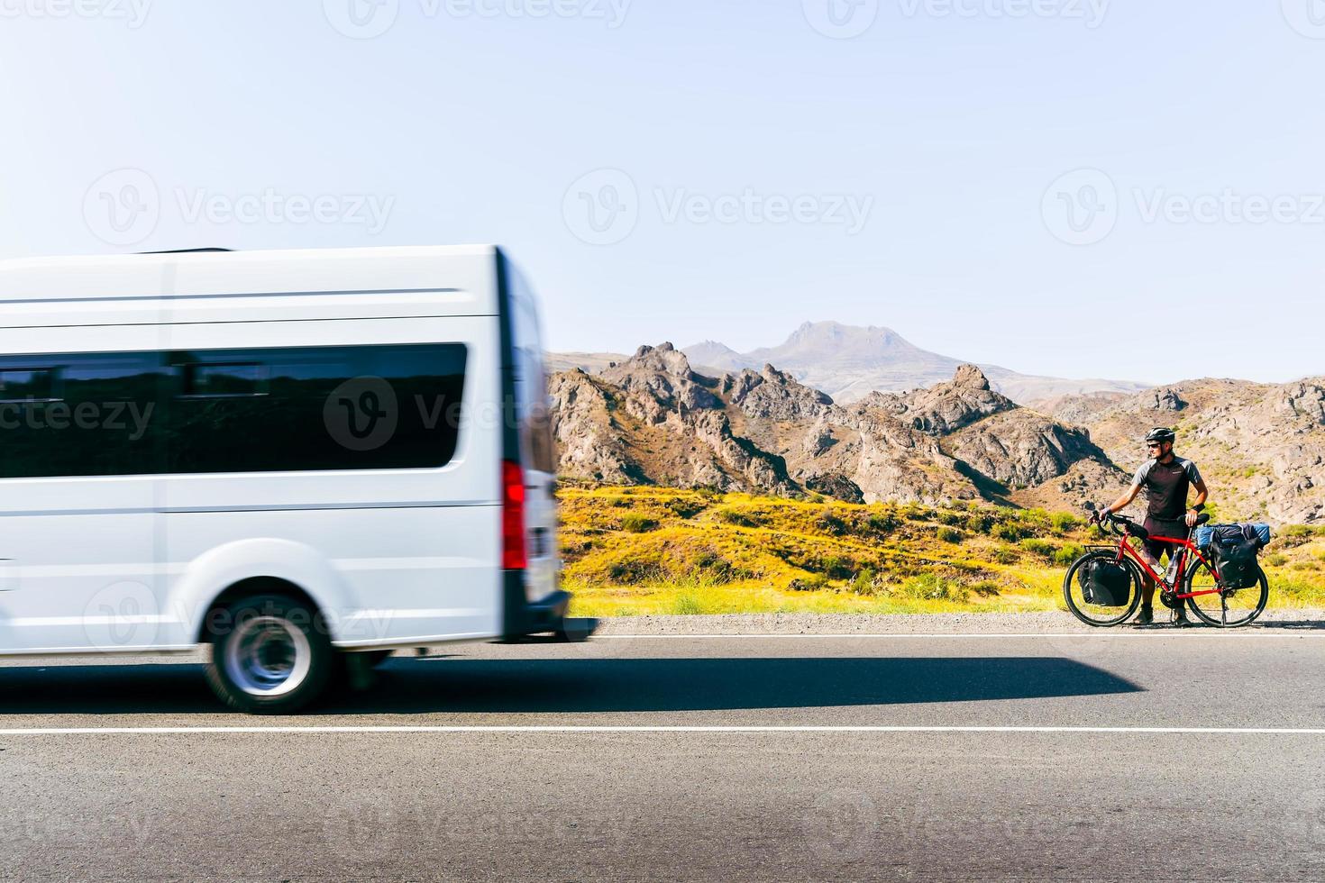 Road side view white van pass male cyclist on side of road in Armenia scenic nature outdoors. Bicycle touring outdoors and bicycle transportation concept photo
