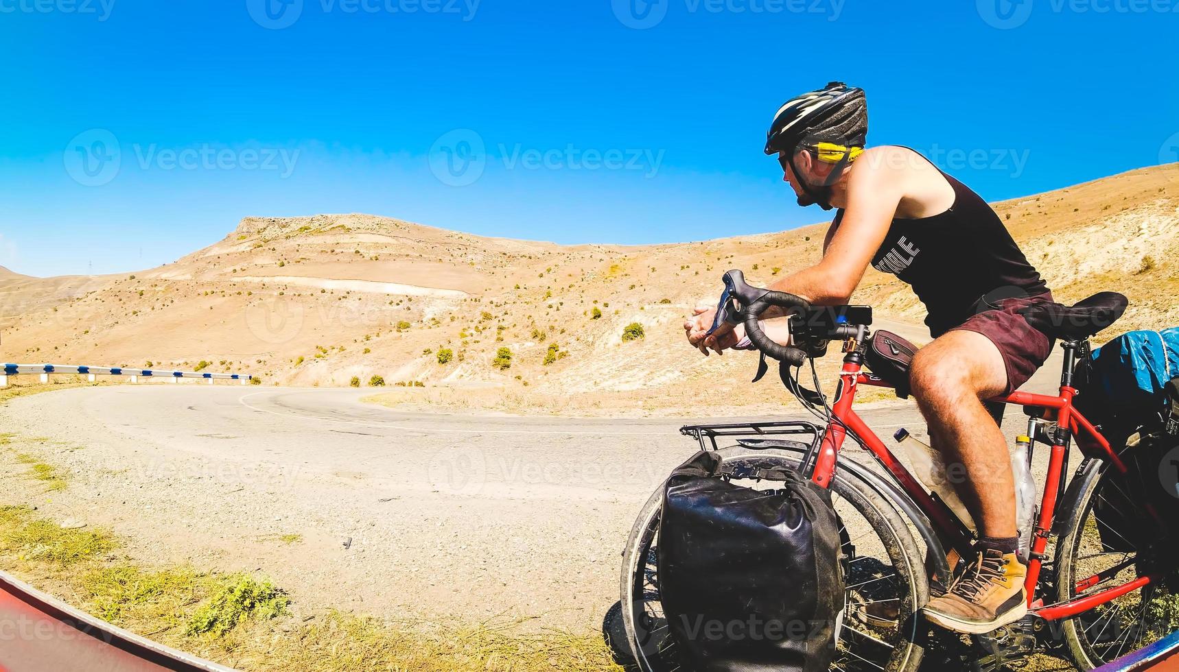 ciclista masculino en un recorrido en bicicleta por una carretera asfaltada al aire libre con vistas a la montaña. viajes de aventura al aire libre. antes de ir cuesta arriba concéntrate pensativo. determinación y desafío foto