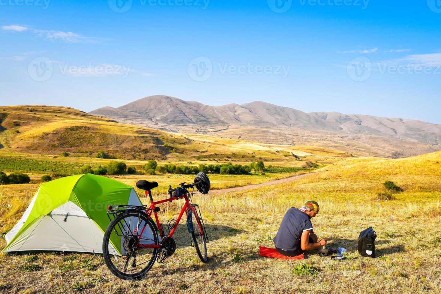 Caucasian person make breakfast early morning by tent solo. Healthy lifestyle and bicycle touring. Ecological travel photo