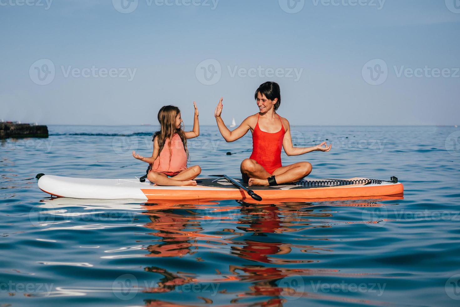 madre e hija haciendo yoga en la tabla de paddle foto