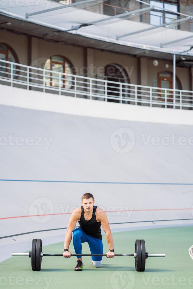 Young guy raises the bar in the stadium, outdoor workout photo