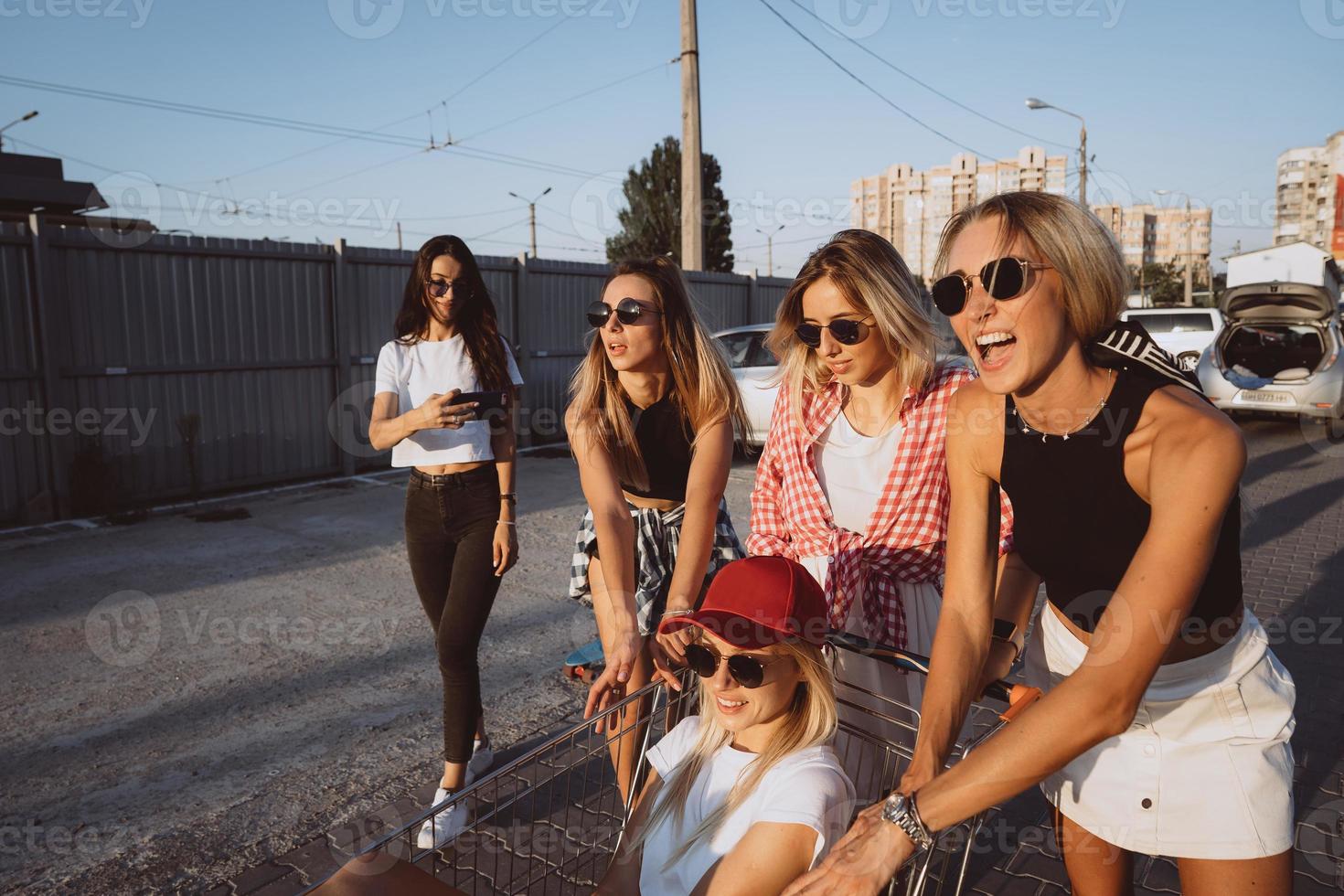 Five young girls have fun with a supermarket cart on a car park photo
