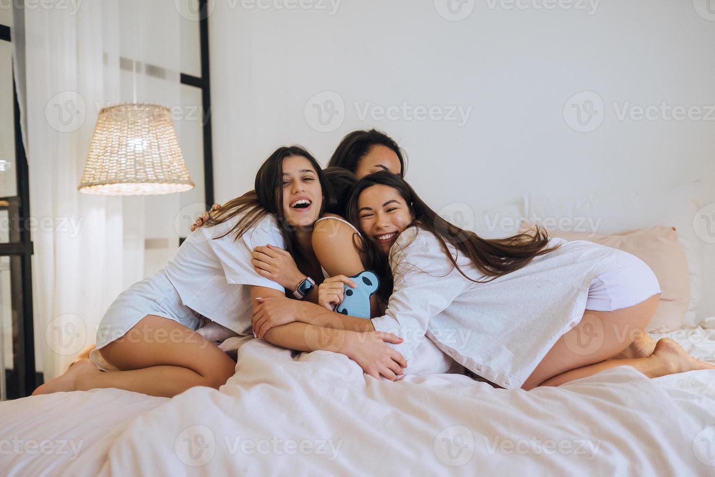 Positive young girls women friends indoors on bed at the hen party at home. photo