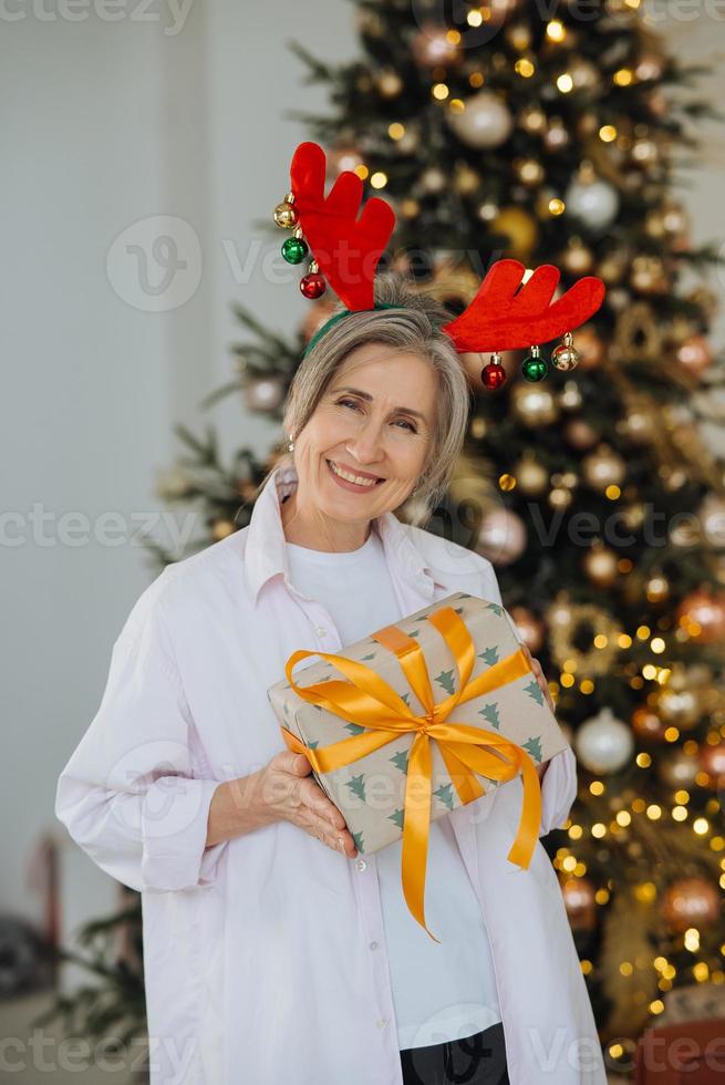 Grandma wearing deer christmas hat. Christmas present in hand . photo