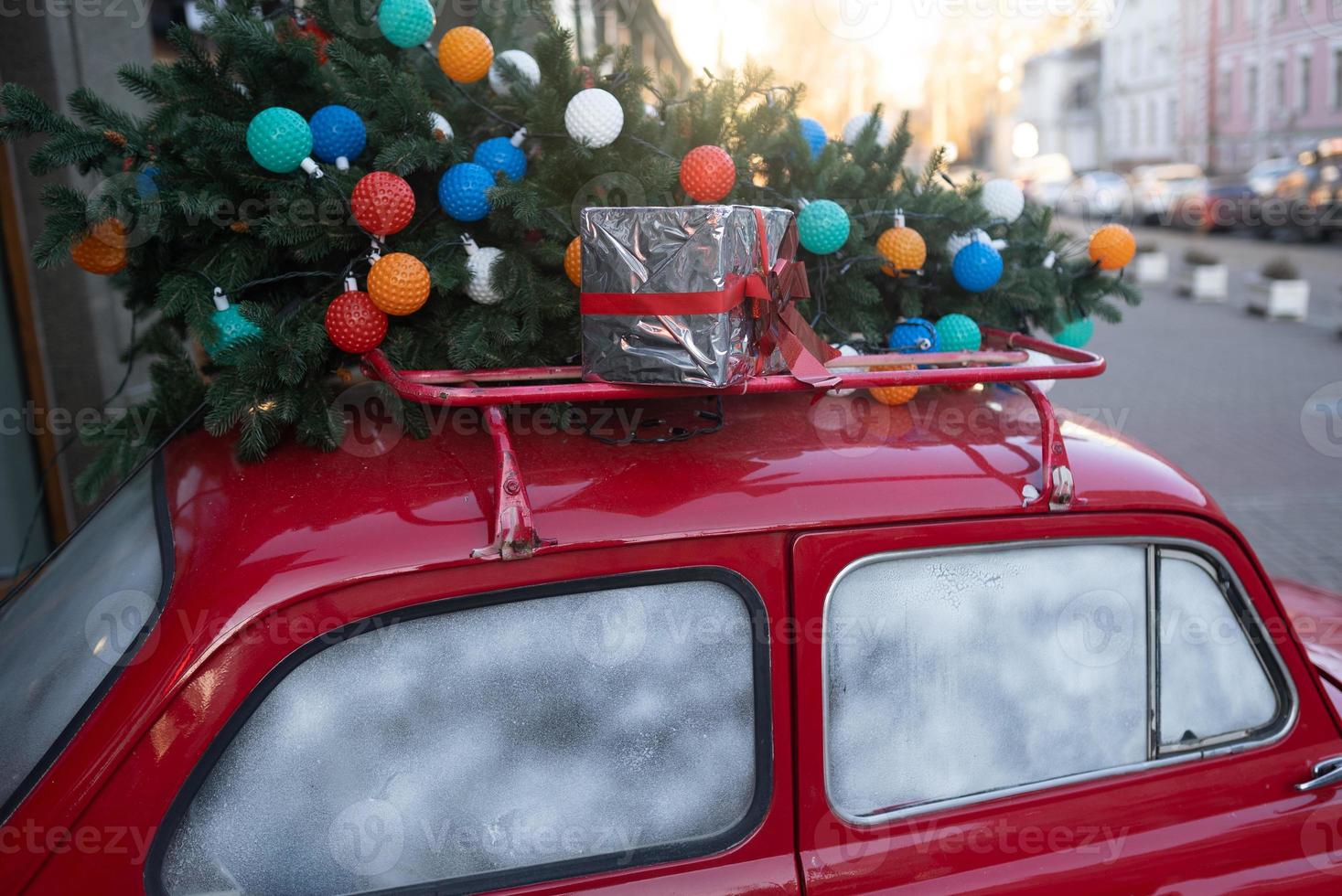 Red retro car with a Christmas tree fir tied to the roof. photo