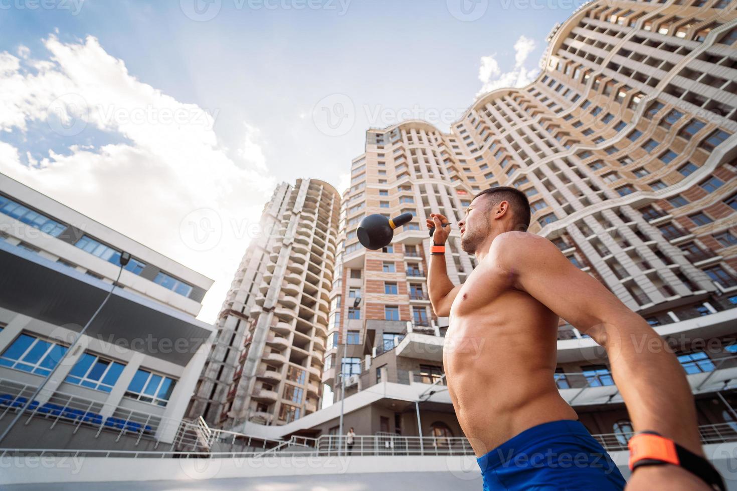 chico deportivo entrenando con pesas rusas en el fondo de un edificio alto. foto